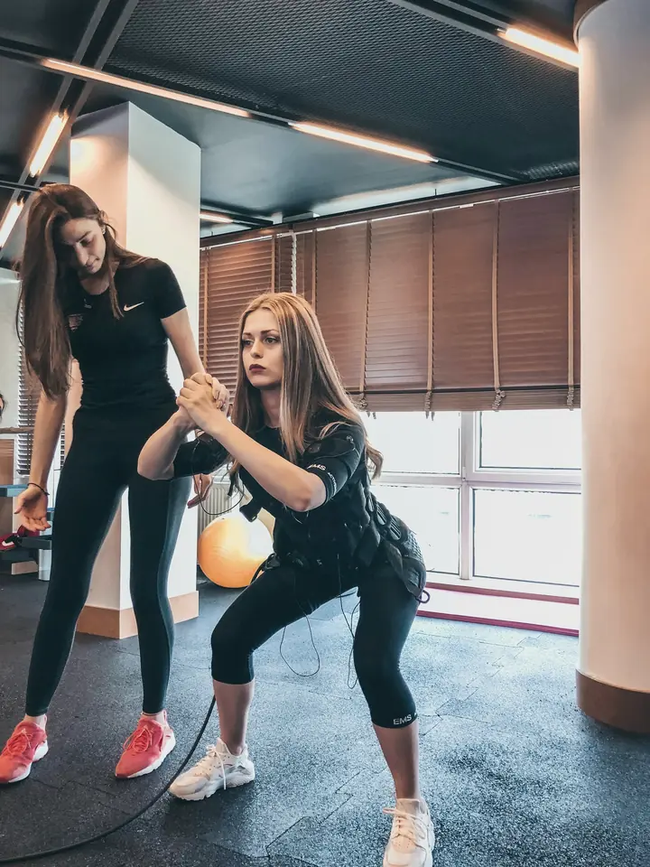A trainer correcting a client's squat in a bright studio