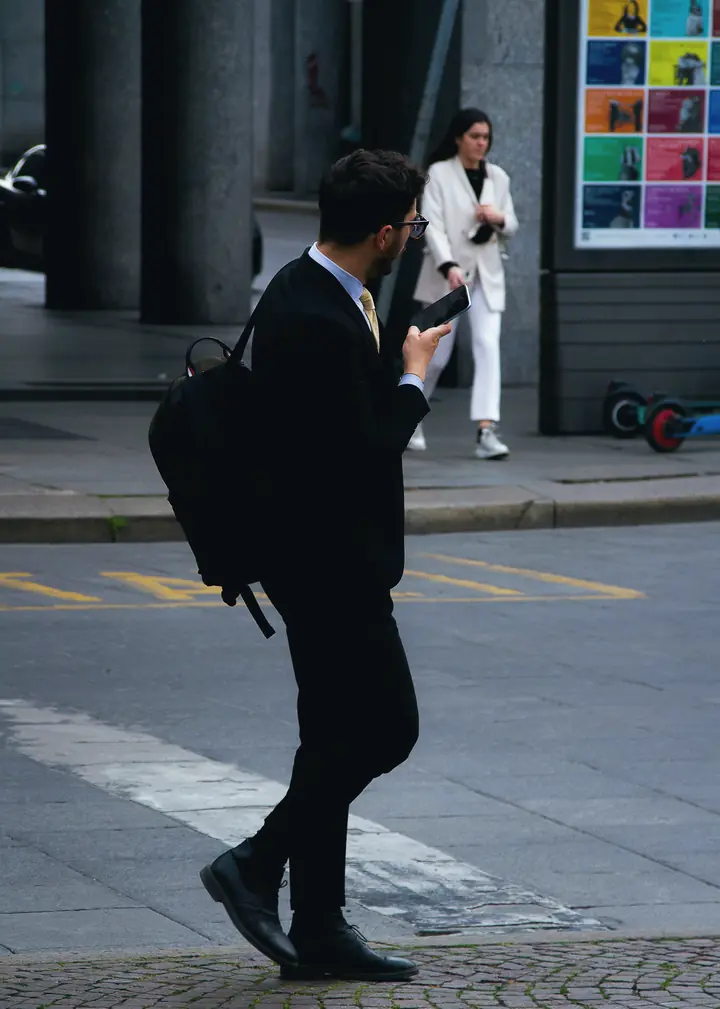 A man in a suit crossing a city street while checking his phone
