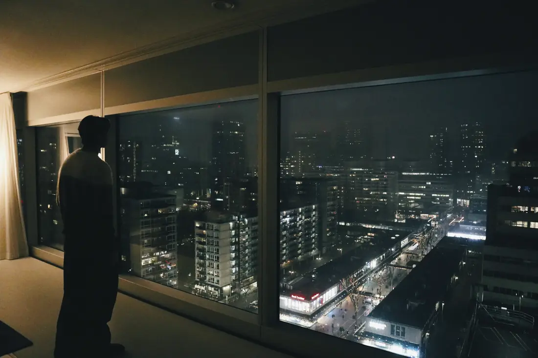 A traveler at a hotel window looking over a city at night
