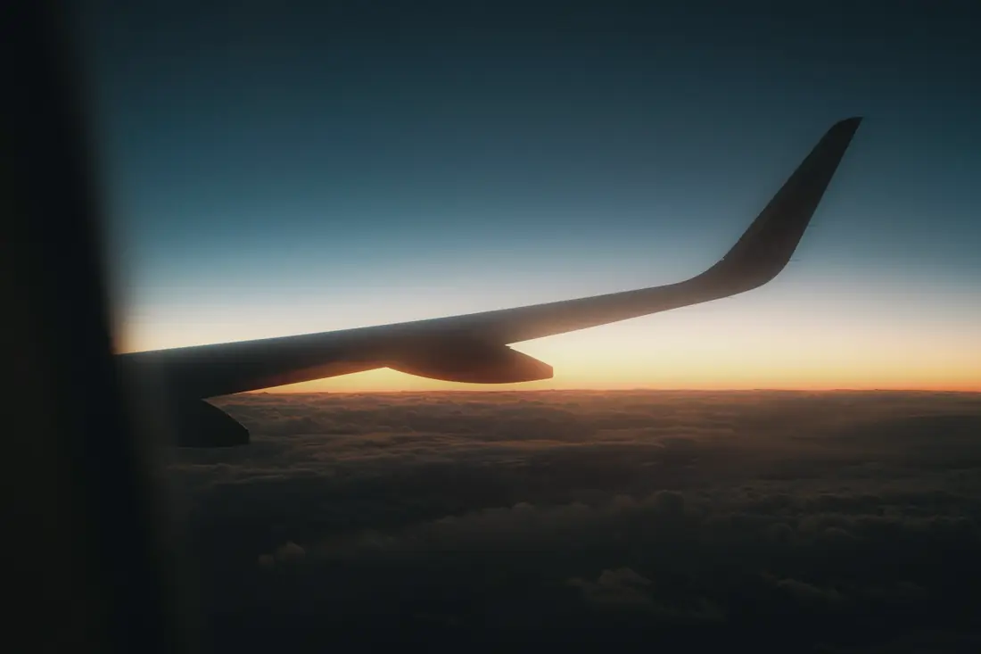 An airplane wing silhouetted against the horizon at dawn